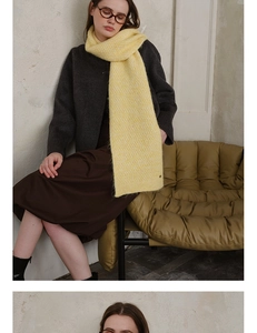 Detail of light yellow knit scarf showing waffle texture and small metal branding tag