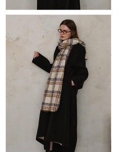 Detail of plaid scarf with tassels styled on a black coat against a beige wall background