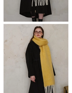 Detail of yellow wool scarf with thick white fringe worn over a black winter coat