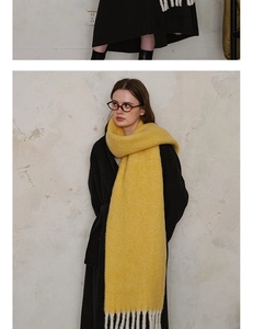 Detail of bright yellow knitted wool scarf with long white fringes on a black winter coat