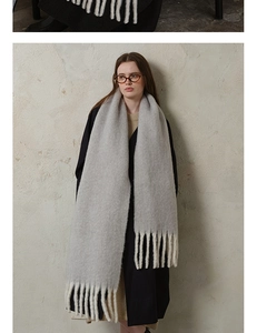 Detail shot of thick light grey wool scarf showing soft knit texture and long fringe design