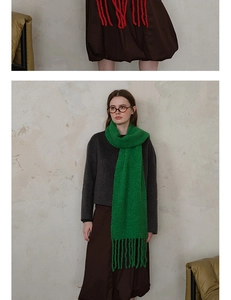 Detail of emerald green wool-blend knitted scarf featuring long tassels and textured knit