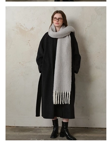 Full-body shot of a thick light grey wool scarf with tassels and a black coat