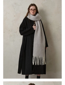 Detailed view of light gray thick wool scarf with tassels paired with a long black coat