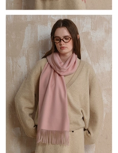 Close-up of a warm pink wool scarf with soft tassels worn over a beige sweater