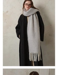 Close-up of thick solid color wool scarf with long tassels on a model in a black coat