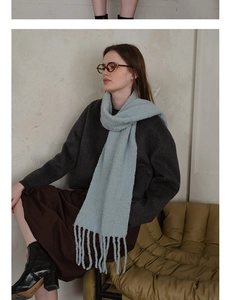 Detail of light blue wool blend scarf showing thick knit texture and long tassel trim