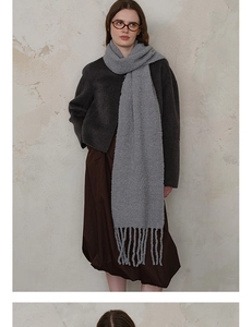 Close-up of the thick knit texture and long tassel details on a soft light grey wool scarf