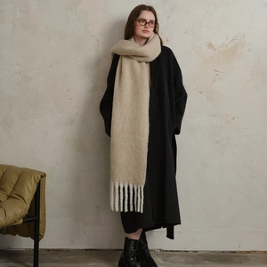 Thick knit beige wool scarf with long tassels paired with a long black winter coat