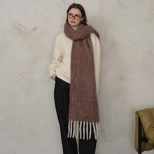Thick brown wool knit scarf with chunky tassels over white sweater for winter warmth