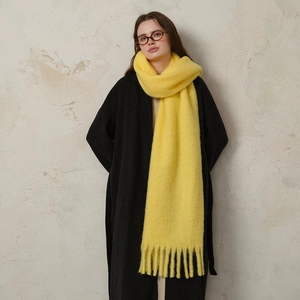 Vibrant yellow wool blend long scarf with fringes worn over a classic black coat