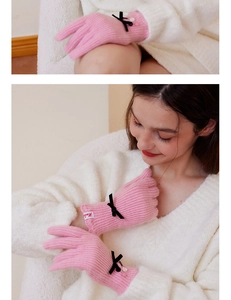 Detail of pink knitted gloves with a black bow, pearl accents and ribbed cuffs
