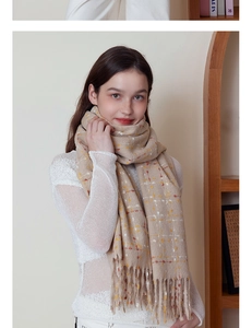 Detail of beige plaid scarf with orange accents and long tassels on soft cashmere-like fabric