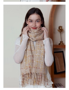 Detail of soft cream plaid scarf with orange accents and tassels on a wooden stand