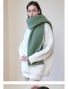 Close-up of thick dark green winter scarf with white wavy stitched edges on a white sweater