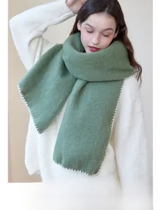 Detail of green knitted scarf featuring soft fuzzy texture and white scalloped edge stitching