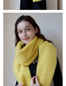 Detail of warm yellow knitted scarf featuring thick texture and black sawtooth edge stitching