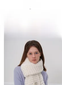 Dettaglio della trama spessa di una sciarpa in maglia beige con etichetta tessuta