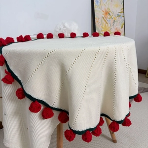 Macro detail of hand-knitted white blanket featuring red pom-poms and green stitched edges