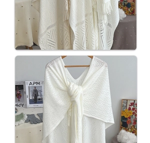 Close-up of white knit shawl with geometric hollow pattern and long fringe trim details