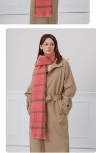 Gros plan d'une écharpe à carreaux rose et vert avec franges sur un trench-coat