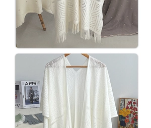 Close-up of white knitted cardigan with fringe hem and geometric镂空 texture detail