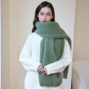 Thick grass green winter scarf with white whipstitch edge worn on a white sweater