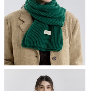 Detail of dark green ribbed knit scarf with woven label on khaki herringbone blazer