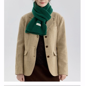 Detail of emerald green chunky knit scarf with white woven label on herringbone blazer