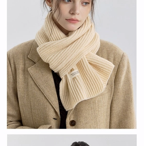 Detail of cream knit scarf featuring vertical rib texture and a text decorative label