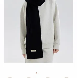 Detail of black knit scarf with vertical ribbed texture and decorative label on model