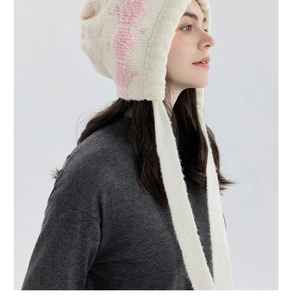 Detail of off-white knit trapper hat showing pink plush embroidery and long earflaps