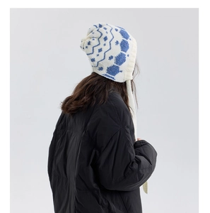Detail of blue and white snowflake knit beanie with earflaps and plush pom-poms