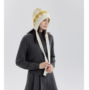 Detail of white knit winter hat featuring yellow patterns and braided tie-up straps