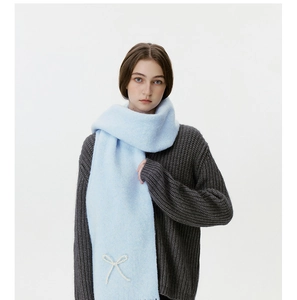 Detail eines hellblauen Winterschals mit weißer 3D-Schleife und weicher Strickstruktur