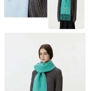 Detailansicht eines mintgrünen Strickschals mit weicher Textur, Fransen und weißer Schleife