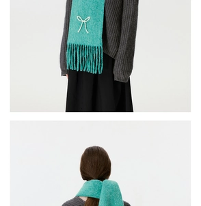 Nahaufnahme eines mintgrünen Strickschals mit weißer Perle und eleganten langen Fransen