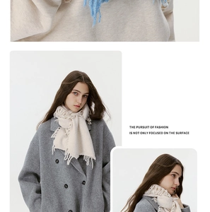 Detailansicht eines cremefarbenen Strickschals mit Fransen auf grauem Wollmantel