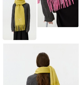 Detail eines gelben Strickschals mit weißer Schleifenstickerei und feinen Fransenverzierungen