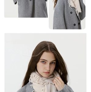 Detail eines weichen cremefarbenen Strickschals mit Fransen und grauem Wintermantel