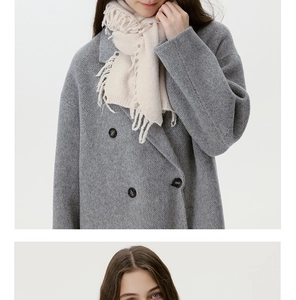 Detailansicht eines cremefarbenen Strickschals mit langen Fransen und grauem Wollmantel