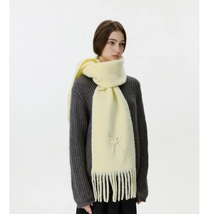 Detail eines cremefarbenen Strickschals mit Perlen-Schleifenmuster und Fransenrand