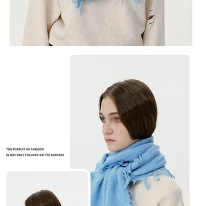 Detail eines hellblauen Strickschals mit Fransen und weicher Textur auf beigem Pullover
