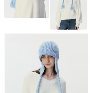 Detail view of light blue cable knit earflap beanie with braided tassel decorations
