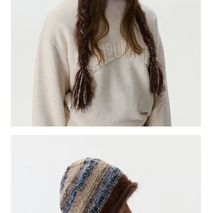 Détail d'un sweat beige avec broderie pelucheuse et un bonnet en maille rayé doux