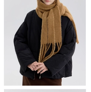 Winter outfit detail featuring a thick camel wool scarf with long fringe and puffer jacket