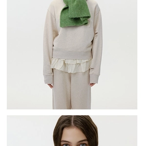 Close-up of wool-blend beige sweatshirt with frayed edges and green knit scarf