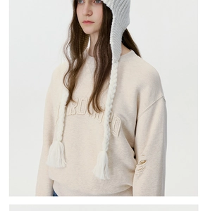 Detail of white chunky knit aviator hat with braided earflaps and beige lettered sweatshirt