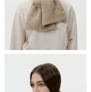 Close-up of wool knit scarf texture in brown grey with a round golden metal logo badge