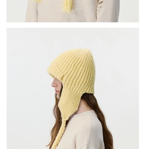 Detail of cream yellow cable knit trapper hat with soft earflaps and braided tassels